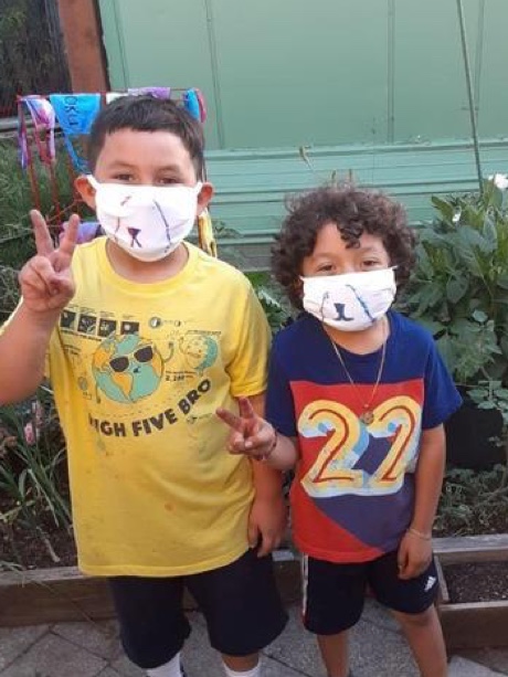 Two young children wearing masks making the peace sign