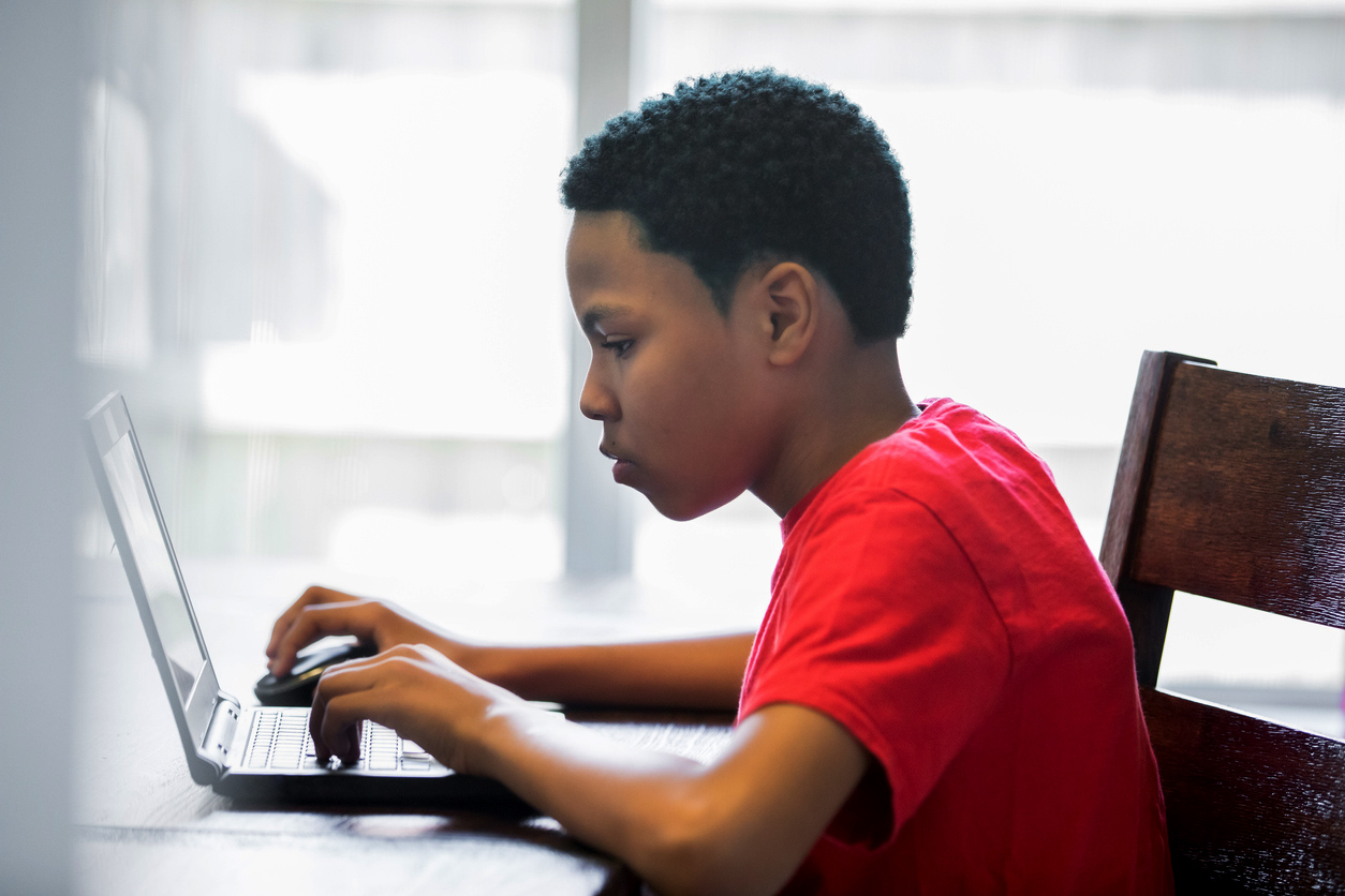 Young teenage boy working on homeschool assignments using laptop at home